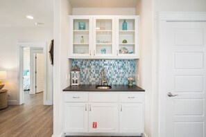 A kitchen with white cabinets, a blue and white tiled backsplash, and a stainless steel sink. - Beach-A-Holic by Silver Sands Vacation Rentals (Port Aransas)