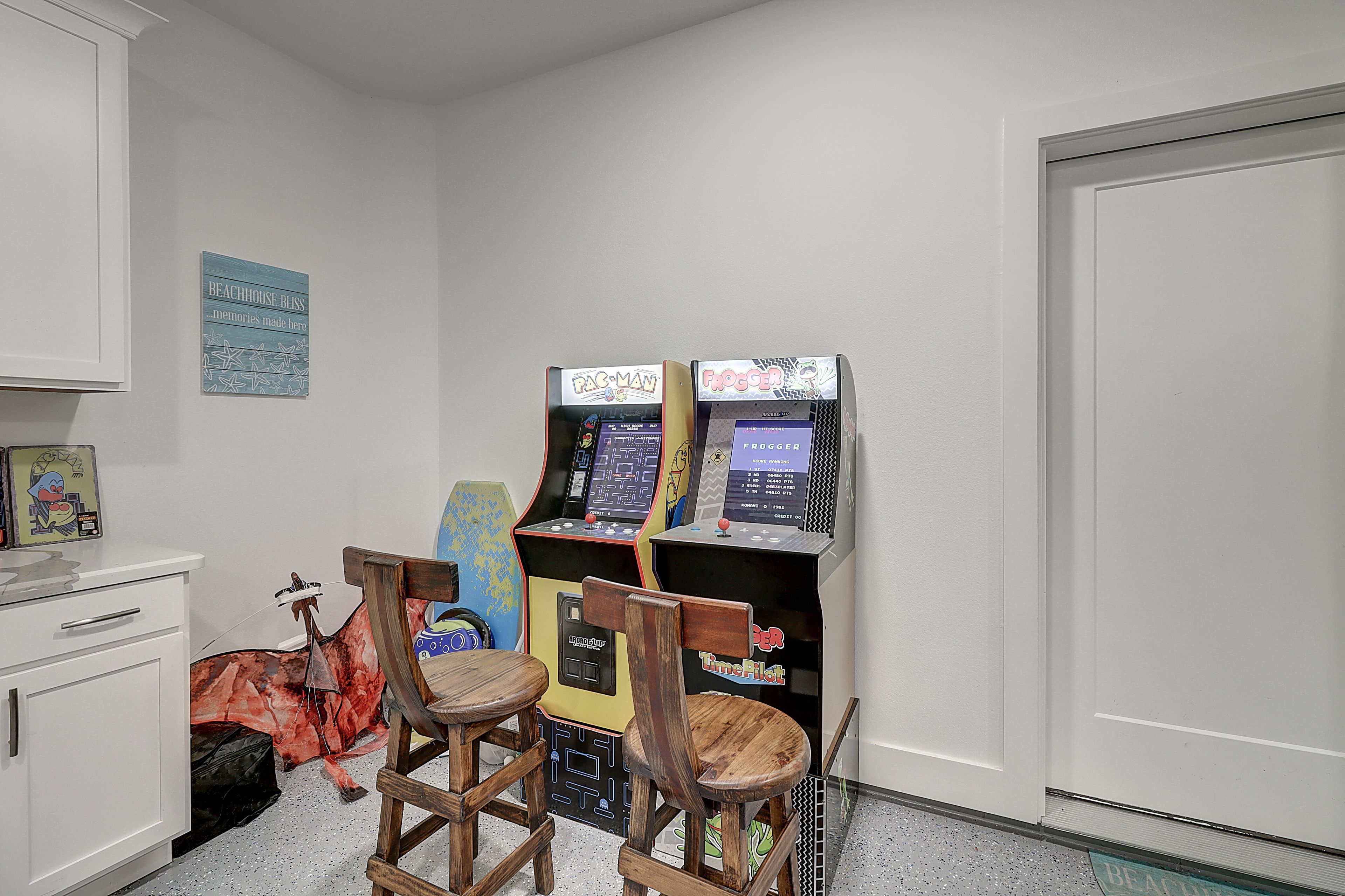 A room with two arcade machines, a wooden chair, and a white cabinet.