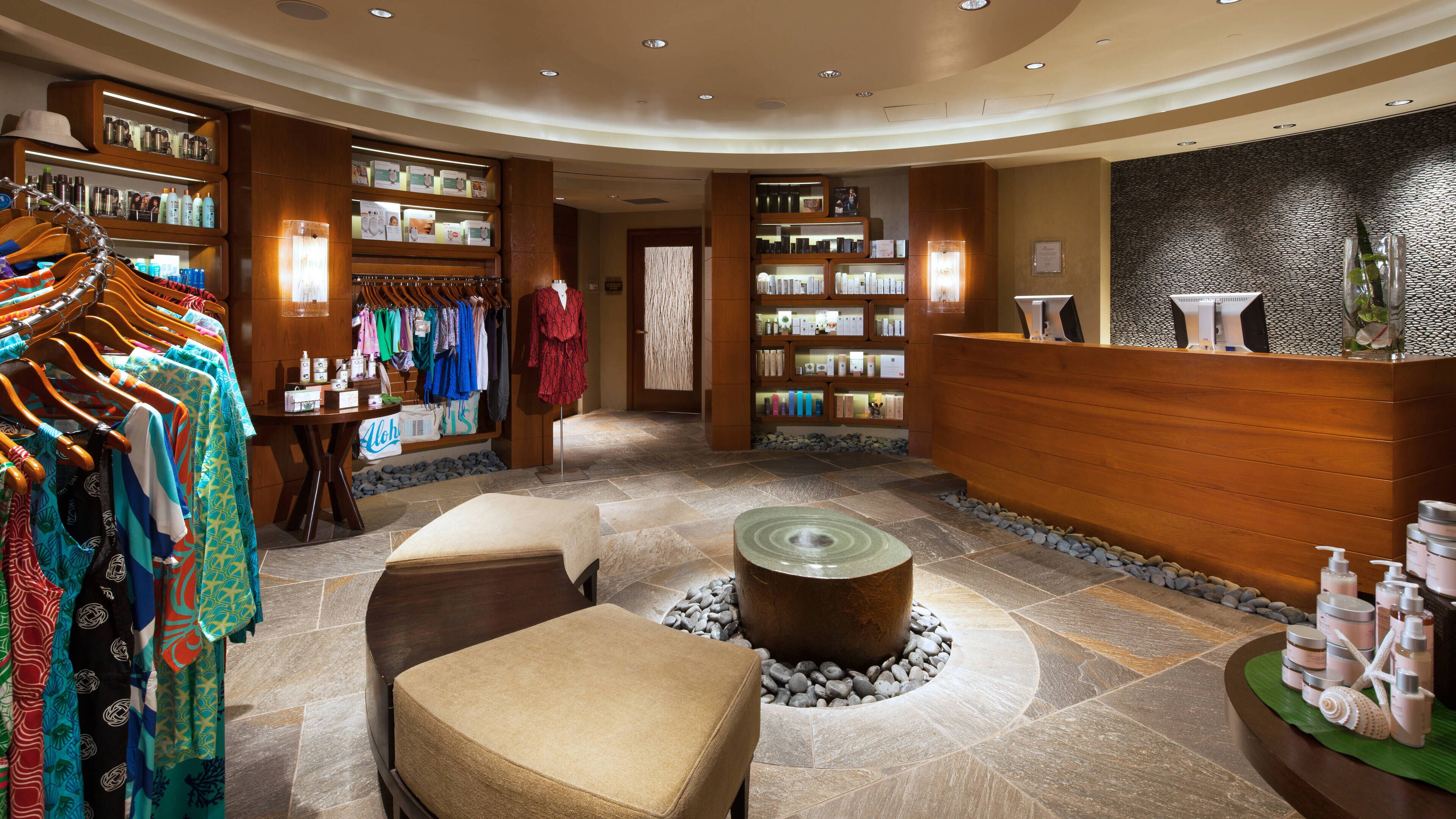 A spa area with a reception desk, shelves with toiletries, a seating area with a round table, and a clothing rack with towels.