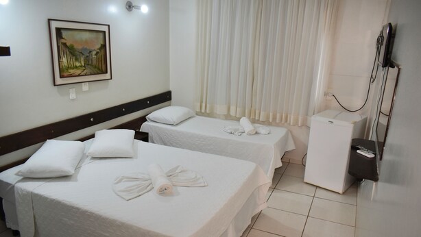 A hotel room with two beds, a small refrigerator, a TV, and a painting on the wall.