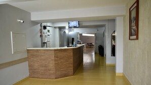 A hotel lobby with a reception desk, a television mounted on the wall, and a corridor leading to other areas.