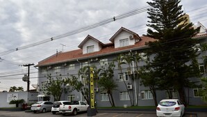 A hotel with a red-tiled roof, multiple windows, and a parking lot with several cars.