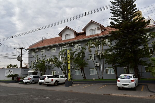 A hotel with a red-tiled roof, multiple windows, and a parking lot with several cars.