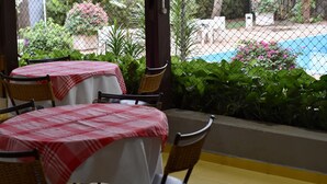 A patio area with tables and chairs, a pool, and lush greenery.
