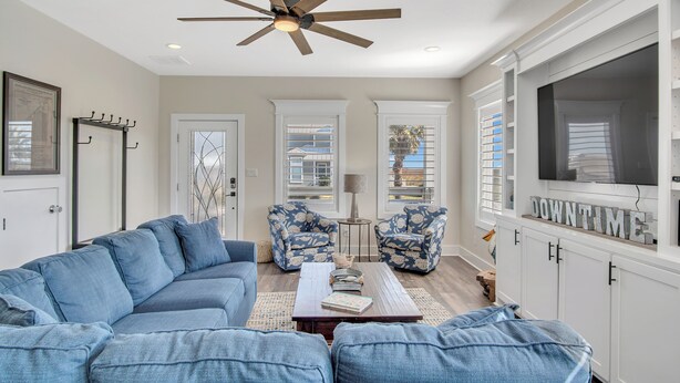 A living room with a blue sofa, two patterned armchairs, a coffee table, a ceiling fan, and a TV mounted on a white cabinet. - Downtime by Silver Sands Vacation Rentals (Port Aransas)