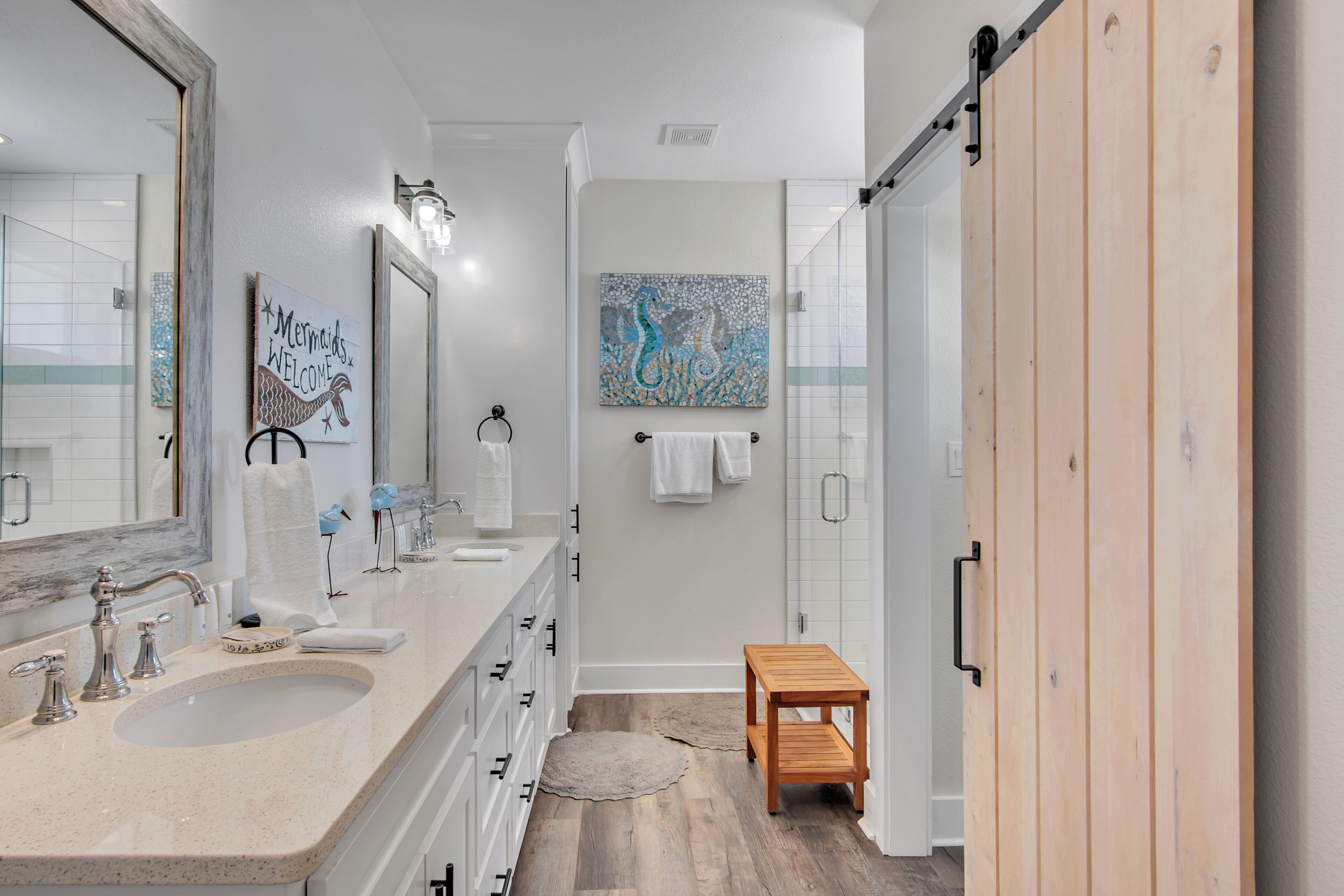 Une salle de bain moderne avec un grand miroir, deux lavabos, un banc en bois et des œuvres d’art accrochées aux murs.