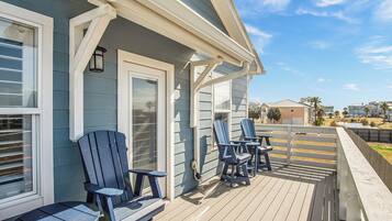A deck with Adirondack chairs and a table, overlooking a residential area.