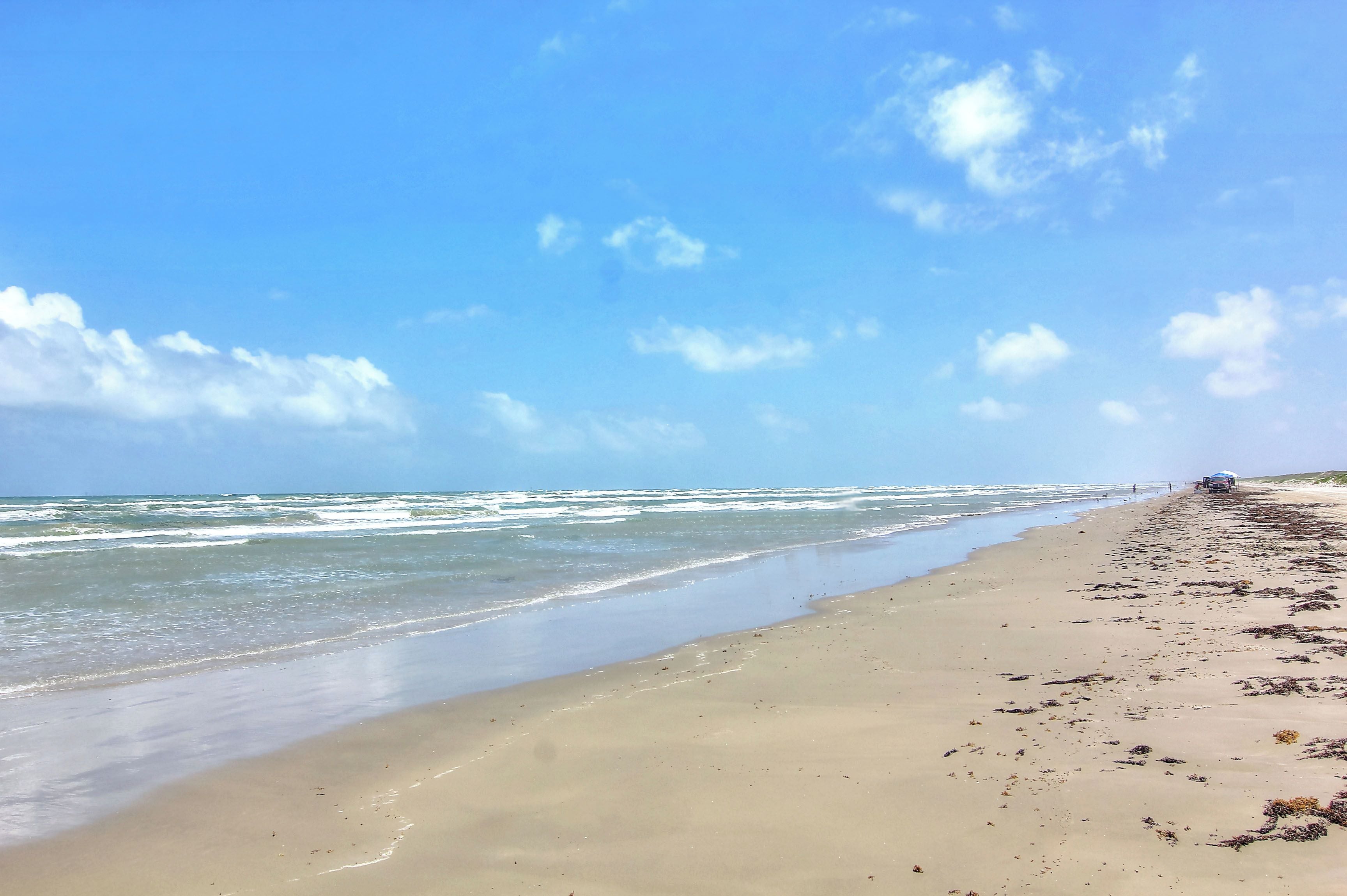Een strand met een heldere lucht, golven en een persoon in de verte.