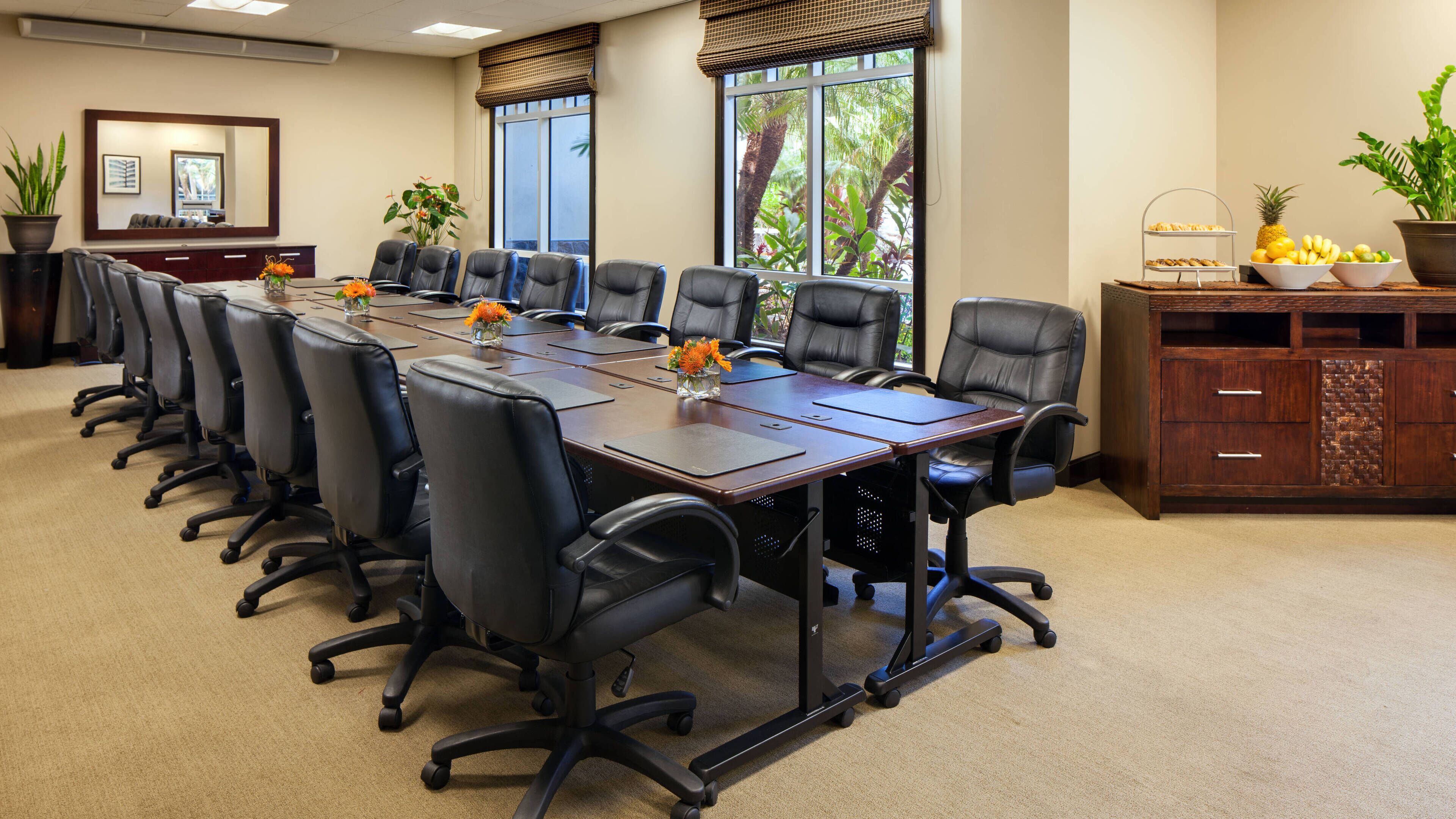 Un salón de conferencias con una larga mesa, varias sillas y un mueble con fruta.