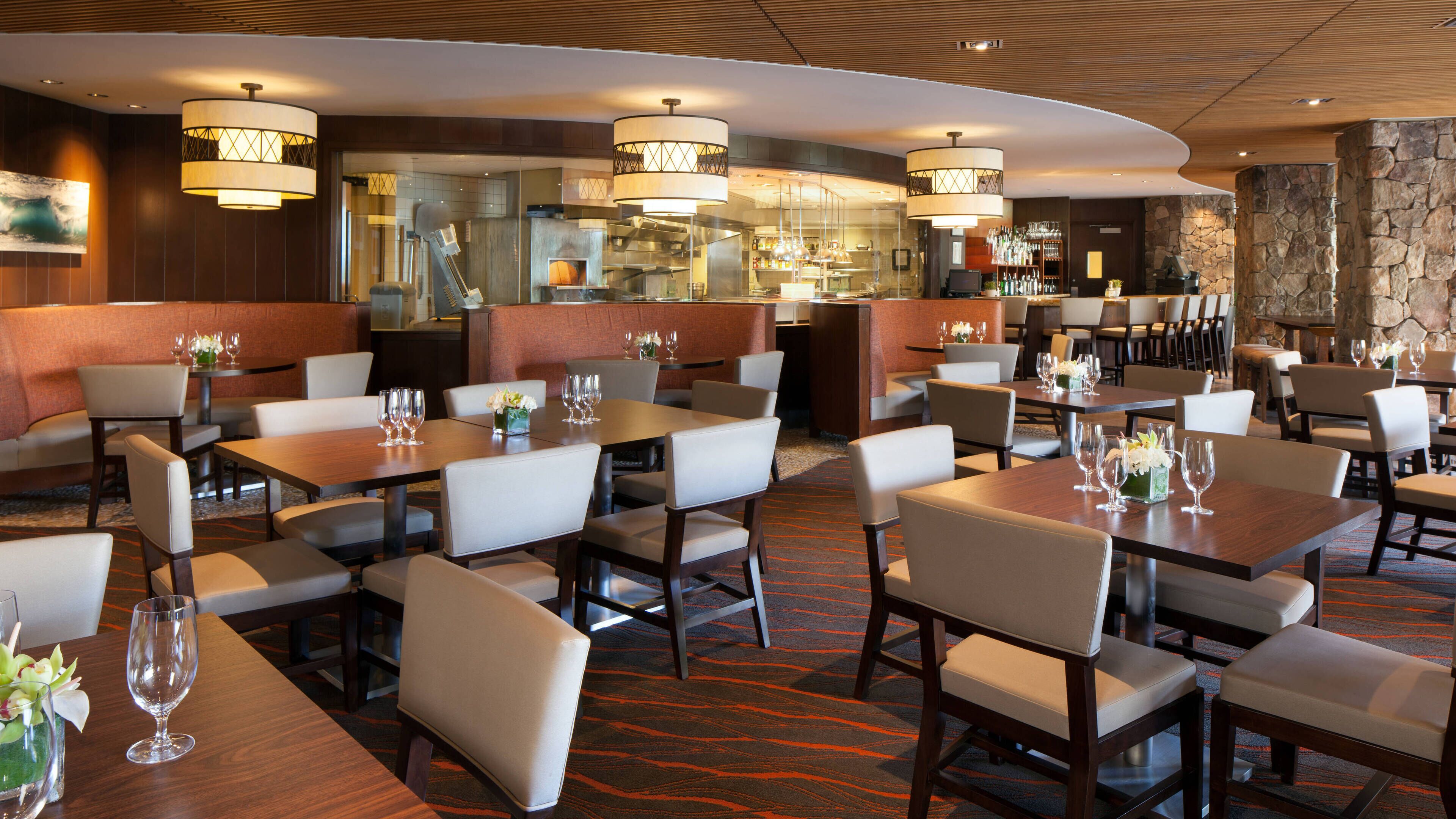 Un restaurante moderno con varias zonas de comedor, incluyendo cabinas y mesas, además de un bar visible a través de una mampara de vidrio.
