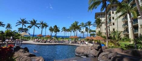 A resort pool with palm trees, lounge chairs, and a view of the ocean.