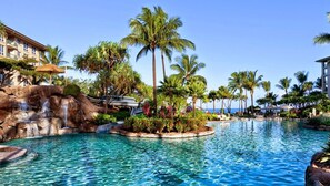 Ein Resort-Pool mit Palmen, einem Wasserfall und einem Gebäude mit Balkonen.