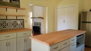 Una cocina con armarios blancos, encimera de madera, horno empotrado y refrigerador de acero inoxidable.