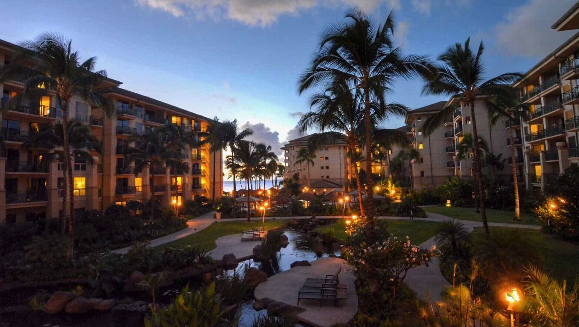 A resort with multiple-story buildings, a central courtyard with a water feature, and palm trees.