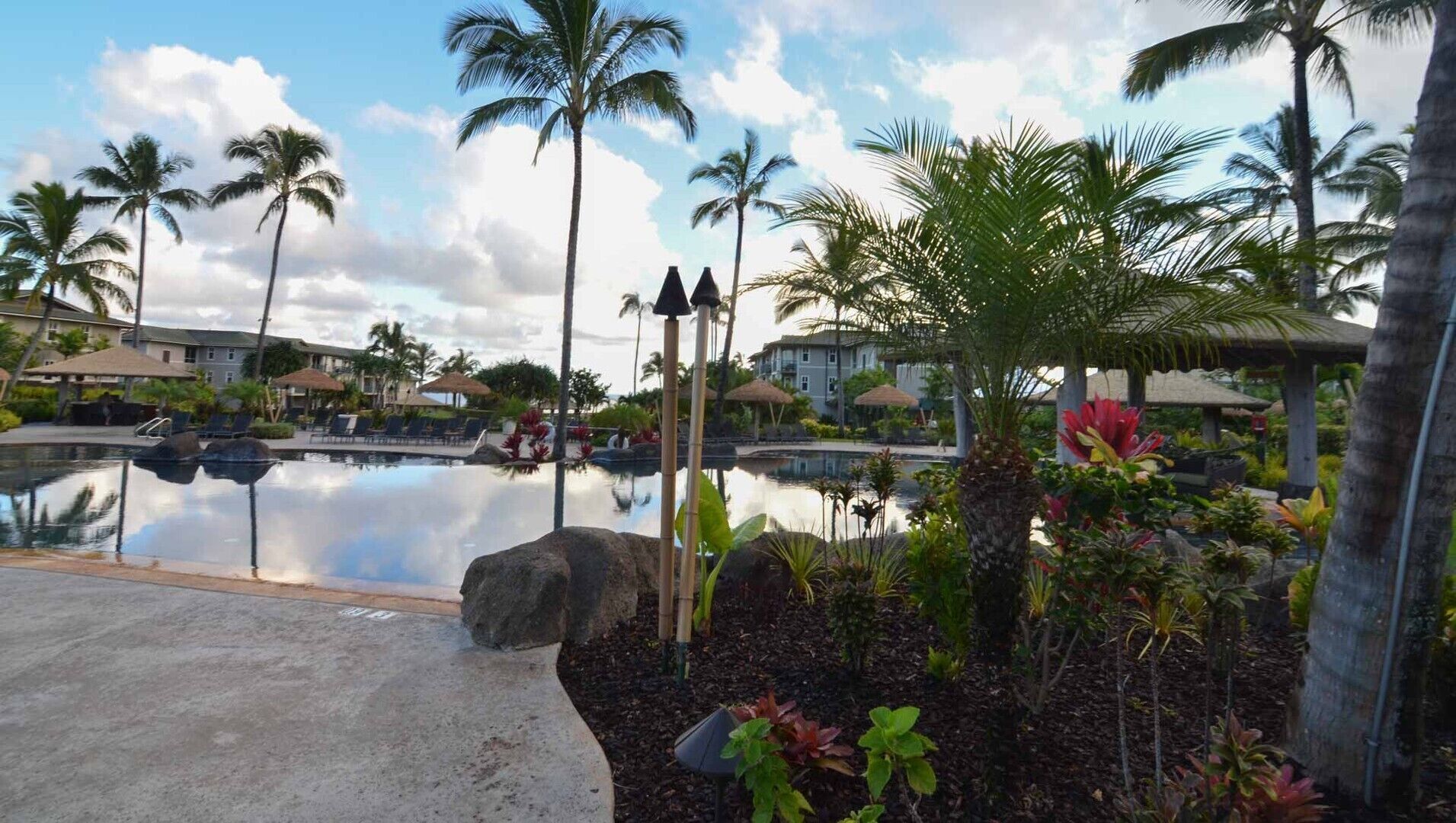 A resort pool area with palm trees, a clear sky, and a reflection in the water.