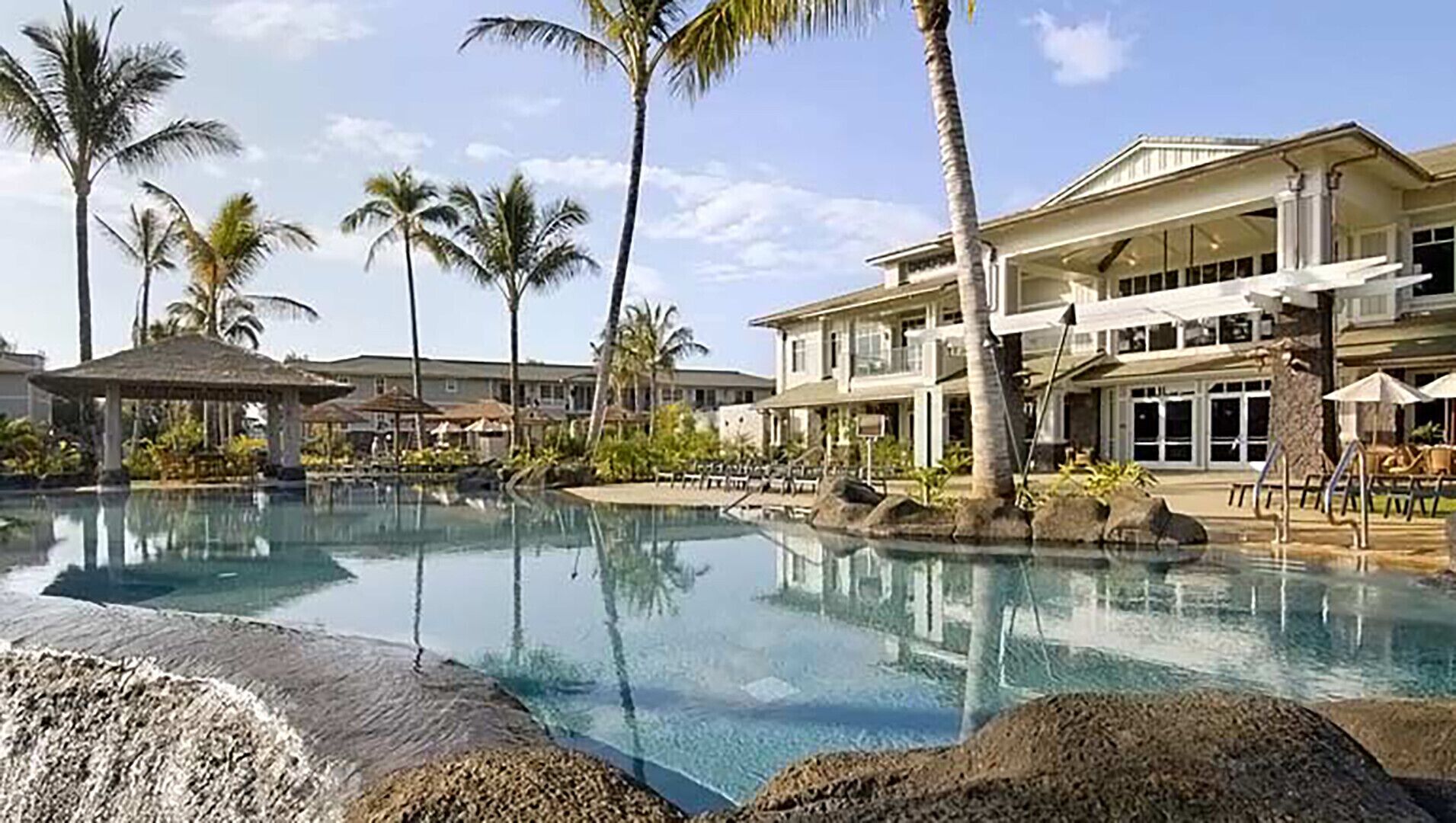 A resort with a large pool, palm trees, and a multi-story building with balconies.