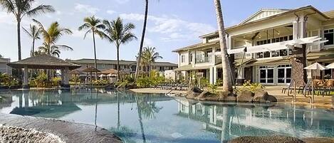 A resort with a large pool, palm trees, and a multi-story building with balconies.