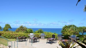 An outdoor patio with tables and chairs, a grill, and a view of the ocean.