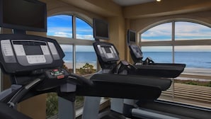 Ein Fitnessraum mit Laufbändern und Trainingsgeräten, große Fenster mit Meerblick.