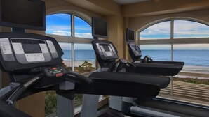 Une salle de sport équipée de tapis de course et d’appareils d’exercice, avec de grandes fenêtres offrant une vue sur l’océan.