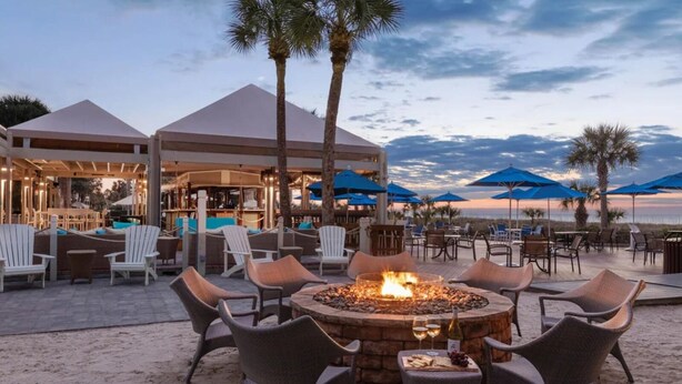 An outdoor seating area with a fire pit, lounge chairs, and umbrellas.