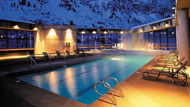 Une piscine intérieure dotée de chaises longues et offrant une vue sur des montagnes enneigées.