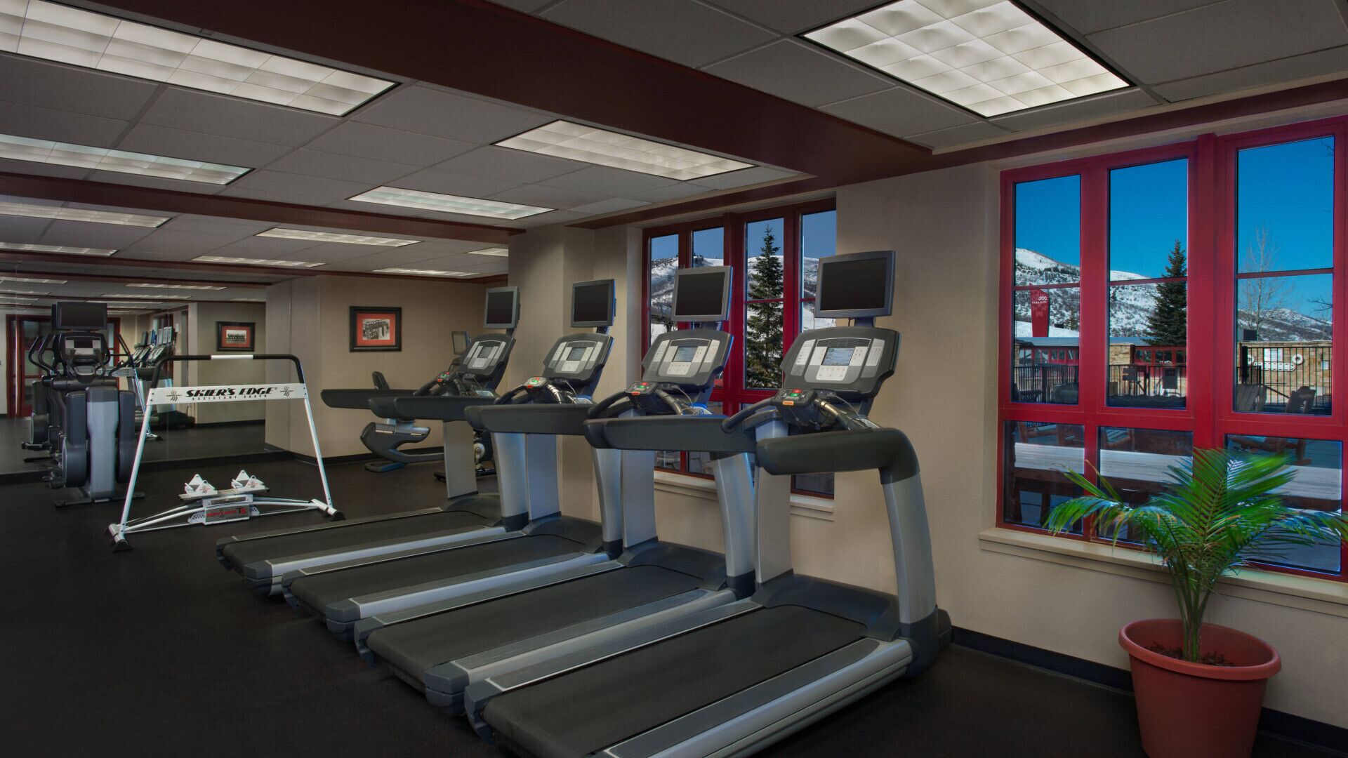 A gym with treadmills, exercise equipment, and large windows with a view of a snowy landscape.