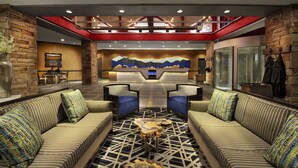 A lobby with a central reception desk, two sofas with patterned cushions, a coffee table, and a large wall mural.