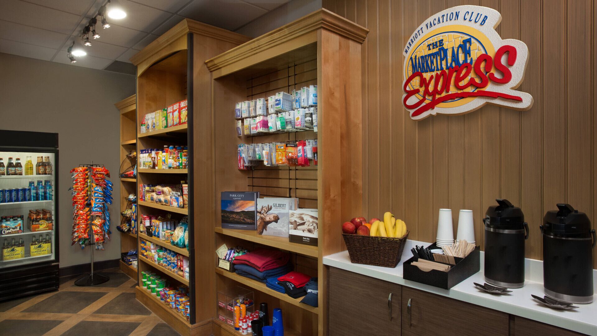 A hotel lobby with a self-service kiosk, shelves stocked with snacks and beverages, and a sign for 'The Marketplace Express'.