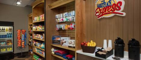 A hotel lobby with a self-service kiosk, shelves stocked with snacks and beverages, and a sign for 'The Marketplace Express'.