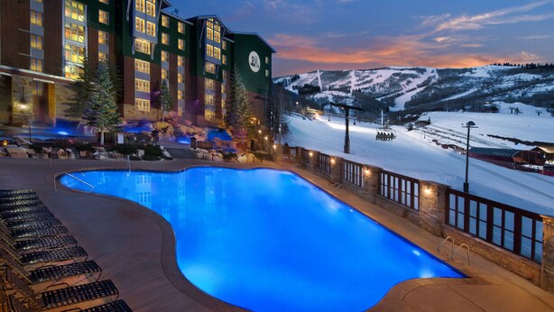 A hotel with a swimming pool, ski lift, and snow-covered mountains in the background.