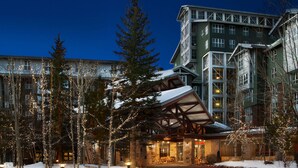 A hotel with a stone facade, a covered outdoor seating area, and a modern building in the background.