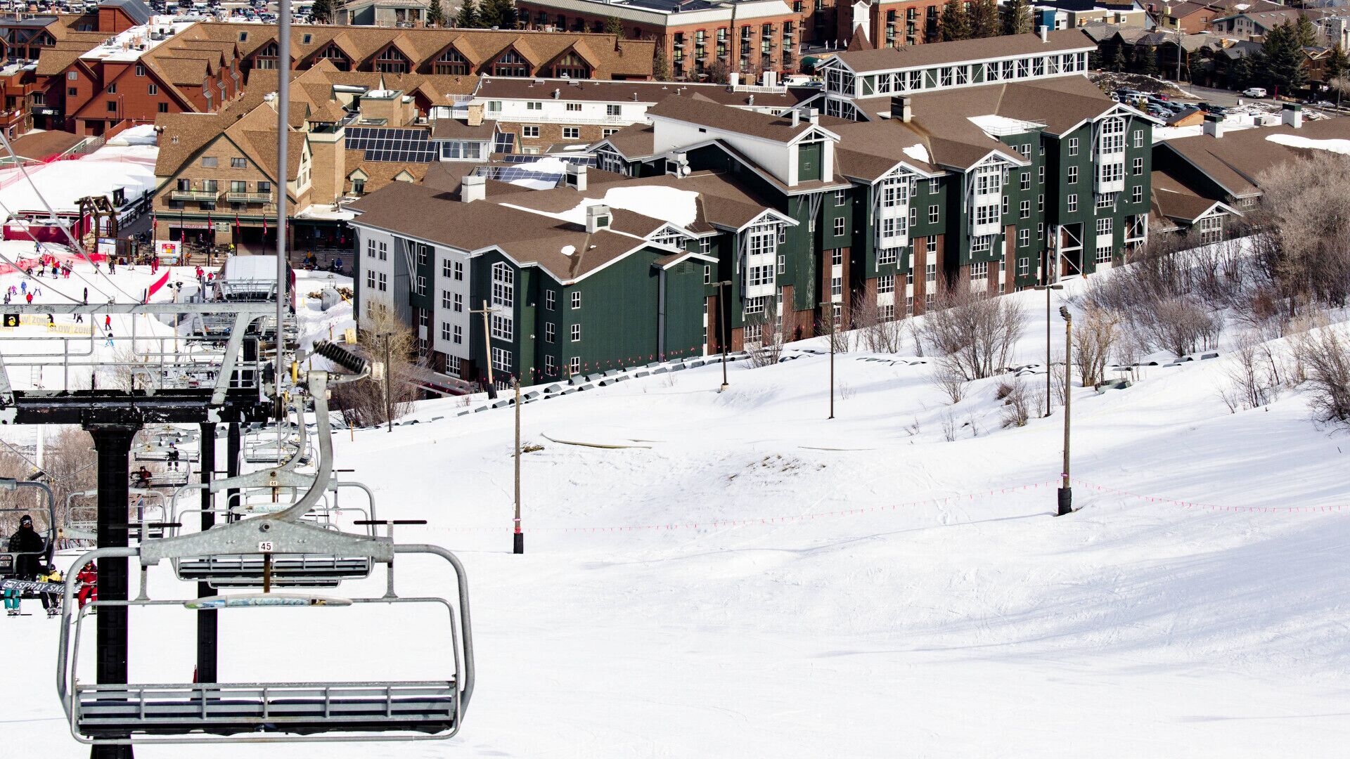 A ski lift with a chairlift and a snowy landscape with buildings in the background.