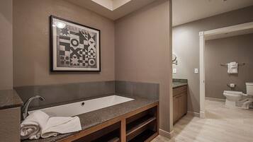Un baño moderno con una bañera independiente grande, un tocador con encimera de granito y una obra de arte abstracta enmarcada en la pared.