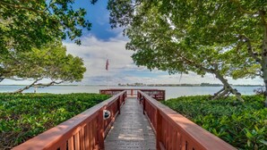 A wooden bridge leading to a body of water, surrounded by lush greenery and an American flag.