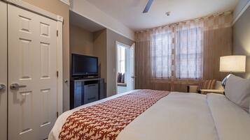 A hotel room with a large bed, a television on a stand, a ceiling fan, and a window with curtains.