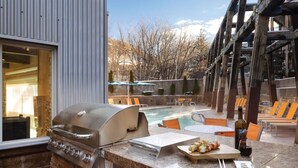 Une terrasse extérieure équipée d’un barbecue, d’une piscine et de chaises longues.