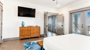 Ein Schlafzimmer mit Bett, Deckenventilator, Fernseher, Holzkommode und Blick durch eine Glastür.