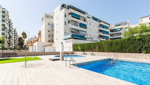 Un moderno edificio de apartamentos con piscina, mobiliario exterior y un jardín bien cuidado.