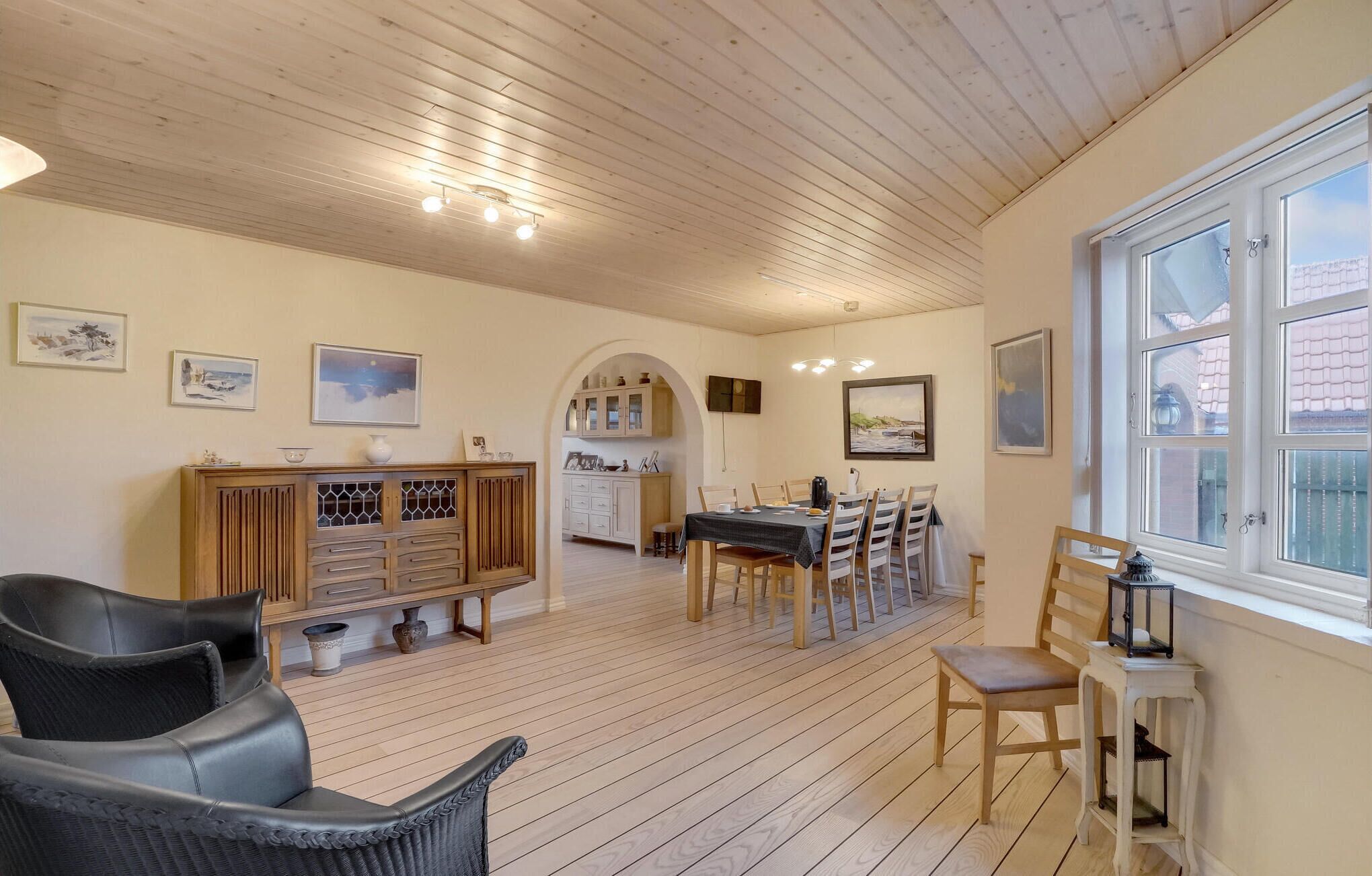 Ein geräumiges Zimmer mit Holzboden, einem Esstisch mit Stühlen, einer Couch und einer Kommode mit Dekoration.