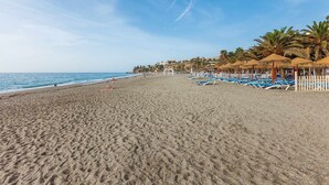Ein Strand mit Reihen von Liegestühlen und Reetdachschirmen, einem klaren Himmel und ruhiger See.