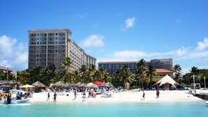Een strandhotel met meerdere verdiepingen, een zandstrand en palmbomen.