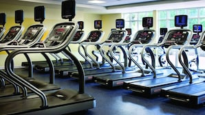 A row of treadmills with digital displays, arranged in a gym with large windows and a blue carpet.