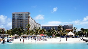 A beachfront hotel with multiple floors, a sandy beach, and palm trees.