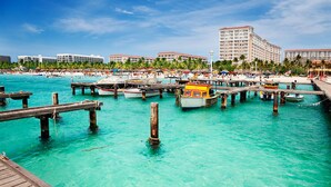 Una zona costanera amb un port esportiu, molls de fusta i una platja amb ombrel·les.