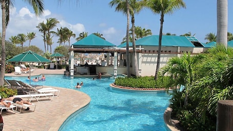 A pool area with lounge chairs, a covered bar area, and palm trees.