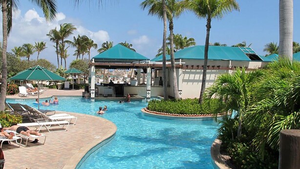 A pool area with lounge chairs, a covered bar area, and palm trees.