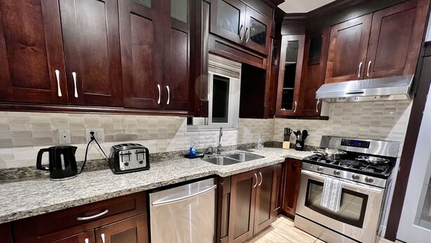 A modern kitchen with dark wooden cabinets, a stainless steel stove, and a granite countertop. - Spacious upper-level unit located on Main St. (Vancouver)