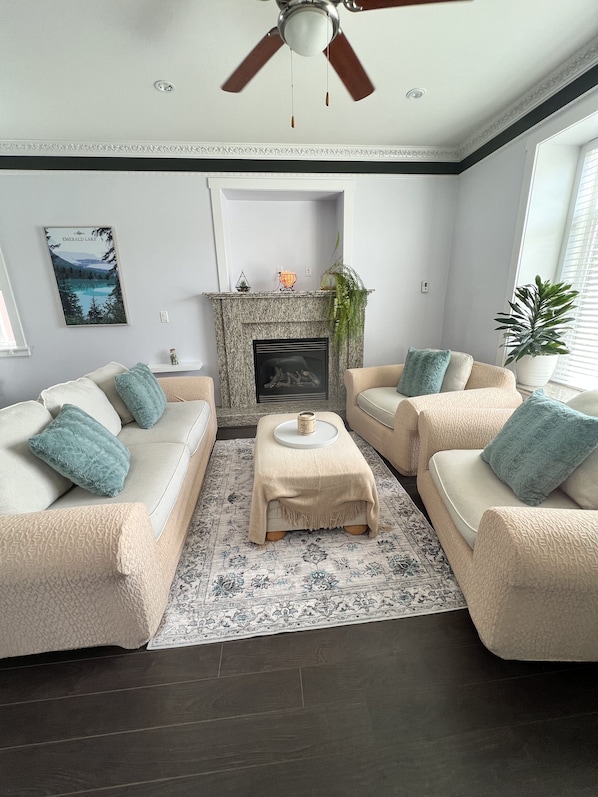 A living room with a fireplace, two beige sofas with blue cushions, a coffee table, and a patterned rug. - Spacious upper-level unit located on Main St. (Vancouver)