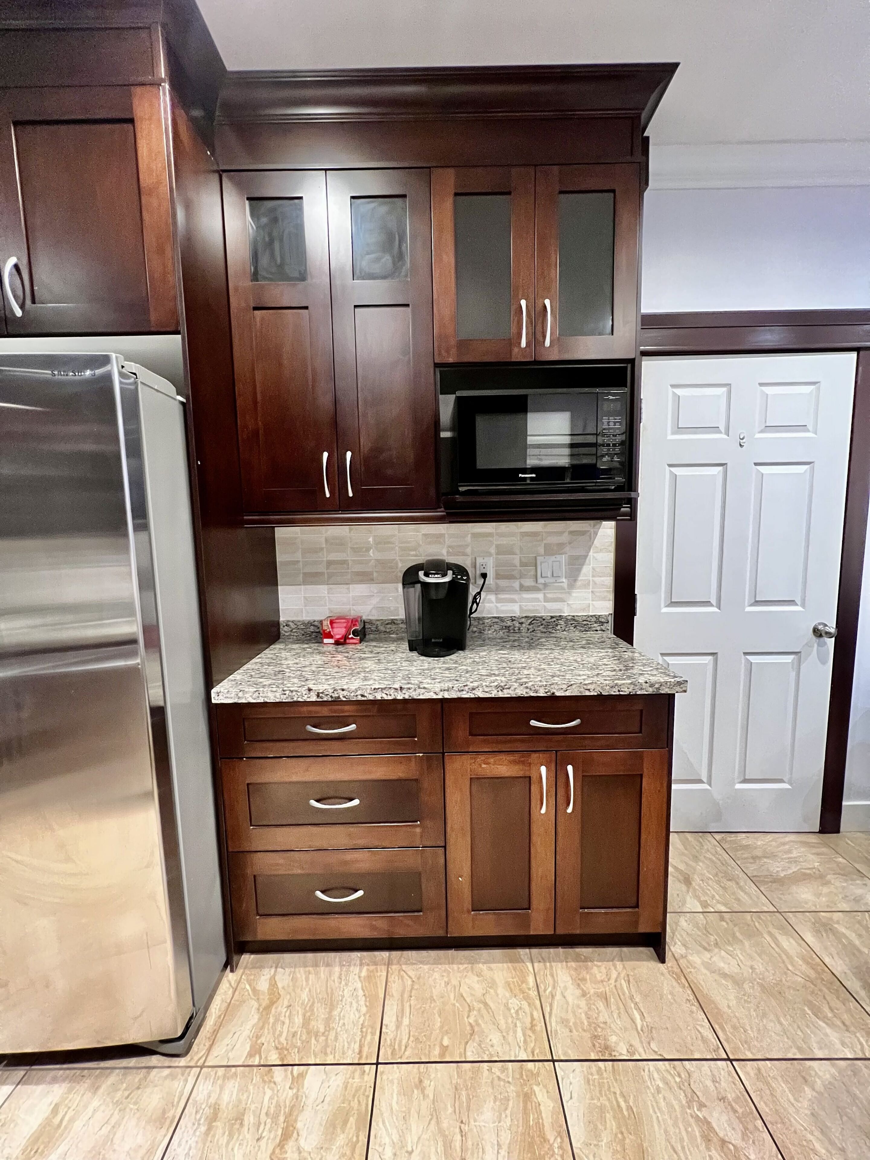 A kitchen with dark wooden cabinets, a stainless steel refrigerator, a microwave, and a coffee maker on the countertop.